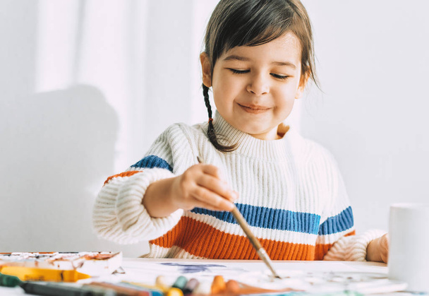 Portrait of cute happy artistic cute little girl drawing with brush at table  - Photo, Image