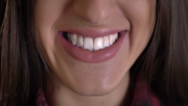 Close-up mond-portret van Kaukasische langharige brunette meisje glimlachend kijken in de camera op zwarte achtergrond. - Video