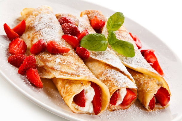 Sweet crepes stuffed with strawberries and cream on white plate - Zdjęcie, obraz