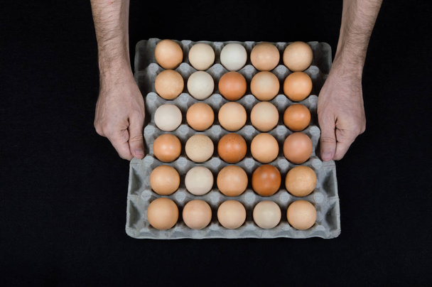 Mężczyzna ręce trzymając jajko tekturowe pudełko pełne kurze jaja na czarnym tle filcu. - Zdjęcie, obraz