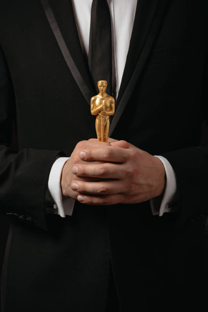 KYIV, UKRAINE - JANUARY 10, 2019: cropped view of man in suit holding oscar award isolated on black - Fotoğraf, Görsel