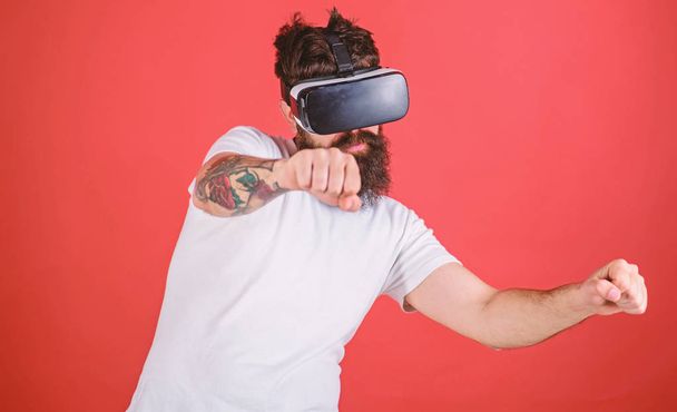 Virtual racing concept. Hipster on confident face driving bike on high speed in virtual reality. Guy play racing game in VR. Man with beard in VR glasses driving motorbike, red background - Photo, Image