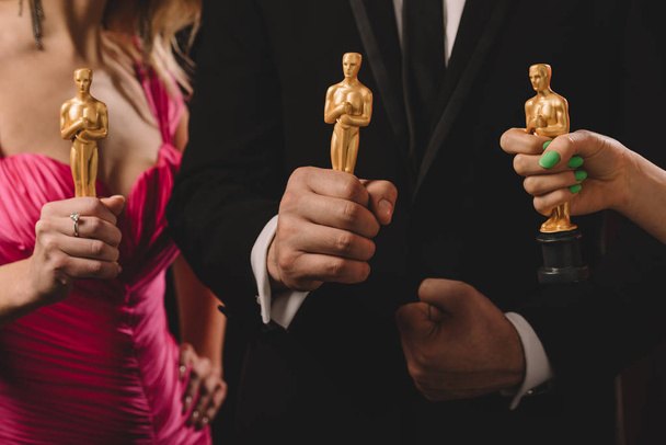 KYIV, UKRAINE - JANUARY 10, 2019: cropped view of women and man holding oscar awards isolated on black - Foto, immagini