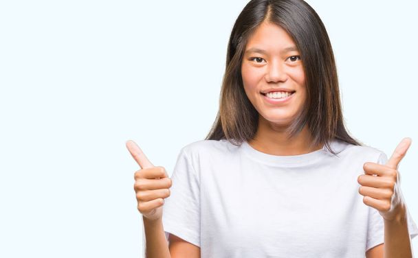 Jeune femme asiatique sur fond isolé signe de succès faisant geste positif avec la main, pouces levés souriant et heureux. En regardant la caméra avec une expression joyeuse, geste gagnant
. - Photo, image