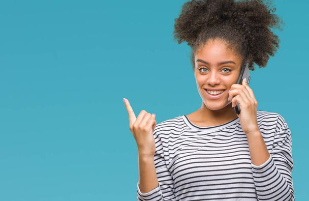 Młody afro american kobieta rozmawia przez telefon na białym tle bardzo szczęśliwy, wskazując z dłoni i palców z boku - Zdjęcie, obraz