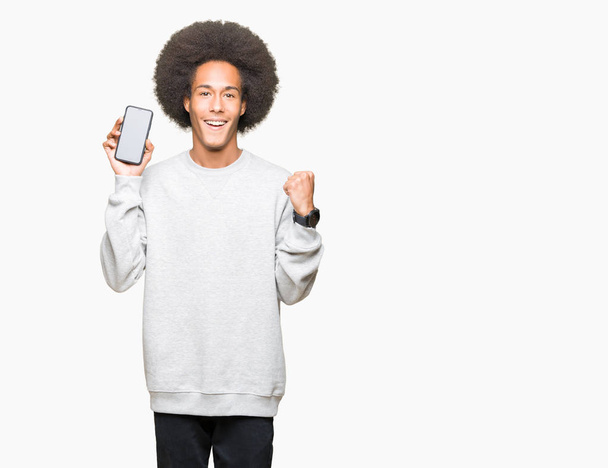 Молодой африканский американец с афроволосами, показывающий экран смартфона, гордо кричащий и празднующий победу и успех очень взволнованный, аплодирующий эмоции
 - Фото, изображение