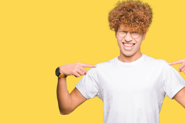 Young handsome man with afro hair wearing glasses looking confident with smile on face, pointing oneself with fingers proud and happy. - Photo, image