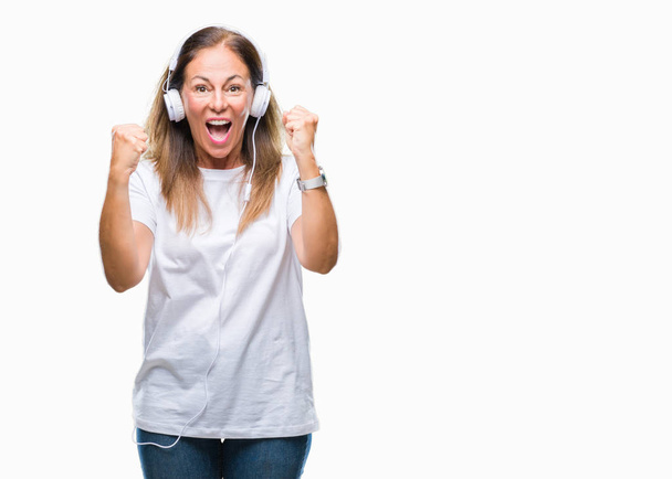 Middle age hispanic woman listening to music wearing headphones over isolated background celebrating surprised and amazed for success with arms raised and open eyes. Winner concept. - Foto, imagen