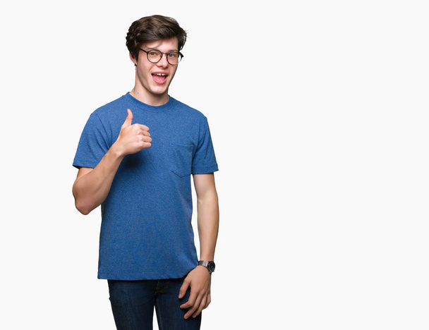Young handsome man wearing glasses over isolated background doing happy thumbs up gesture with hand. Approving expression looking at the camera with showing success. - Фото, изображение