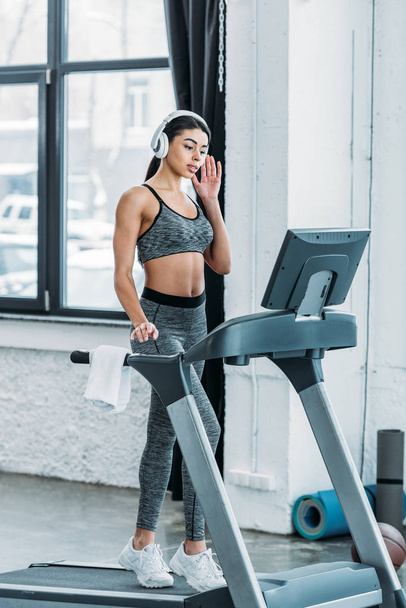 sporty african american girl in headphones exercising on treadmill in gym - Fotó, kép