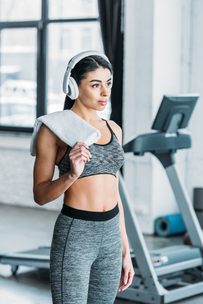 attractive young african american sportswoman in headphones holding towel and looking away in gym  - Φωτογραφία, εικόνα