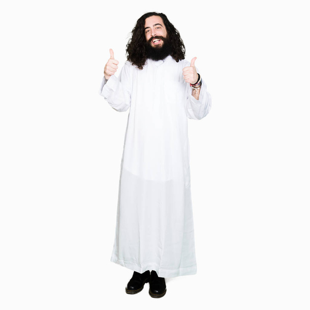 Человек в костюме Иисуса Христа знак успеха делает позитивный жест рукой, большой палец вверх улыбается и счастлив. Глядя в камеру с веселым выражением лица, жест победителя
. - Фото, изображение
