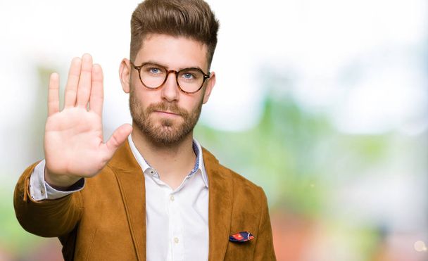 Young handsome business man wearing glasses doing stop sing with palm of the hand. Warning expression with negative and serious gesture on the face. - Photo, Image