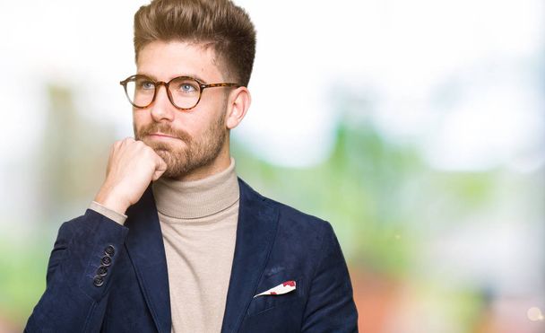 Mladý pohledný obchodní muž nosí brýle s rukou na bradě přemýšlet o otázce, zamyšlený výraz. Usmívající se zamyšlenou tváři. Pochybnost koncept. - Fotografie, Obrázek