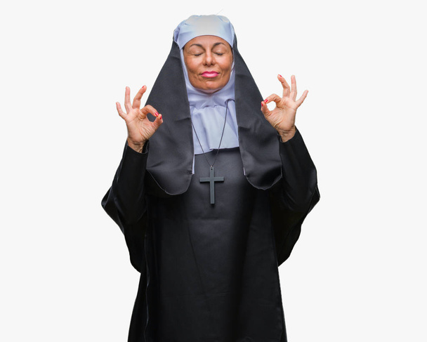Mujer religiosa católica cristiana de mediana edad sobre fondo aislado relajarse y sonreír con los ojos cerrados haciendo gesto de meditación con los dedos. Concepto de yoga
. - Foto, Imagen