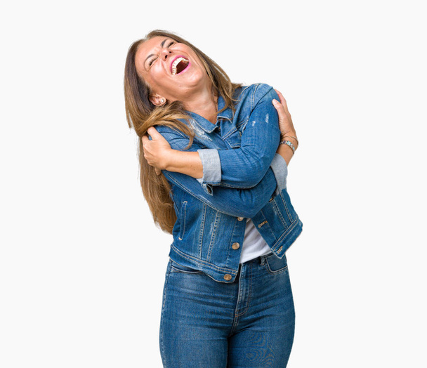 schöne Frau mittleren Alters in lässiger Jeansjacke über isoliertem Hintergrund, die sich glücklich und positiv umarmt, selbstbewusst lächelnd. Selbstliebe und Selbstfürsorge - Foto, Bild