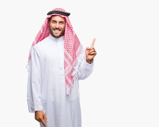 Young handsome man wearing keffiyeh over isolated background with a big smile on face, pointing with hand and finger to the side looking at the camera. - Photo, Image
