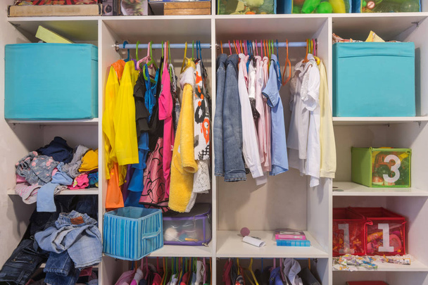 Відкрита шафа з речами та іграшками в дитячій кімнаті
 - Фото, зображення