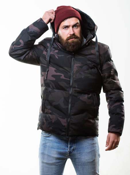 Guy wear hat and black winter jacket. Comfortable winter outfit. Winter stylish menswear. Man bearded stand warm camouflage pattern jacket parka isolated on white background. Hipster winter fashion - Fotó, kép