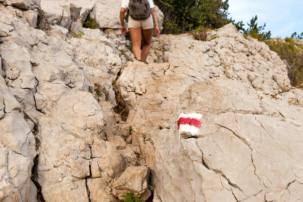 Hiking trail sign on rock and tourist woman walking on path - Foto, Imagen