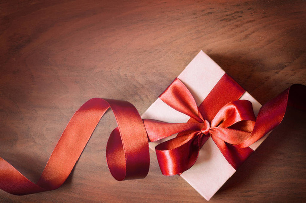 White gift box and red ribbon with tag on wood background. Vintage gift box on wooden board with space for text. - Fotoğraf, Görsel