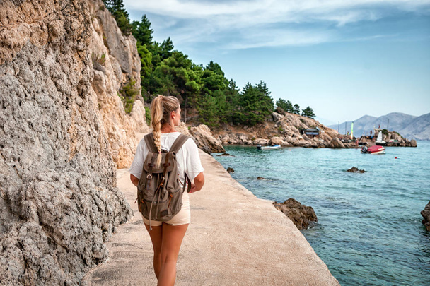 Tourist woman with backpack walking along sea shore, discovering while traveling - Foto, Imagen