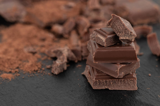 Broken chocolate pieces and cocoa powder on a dark background. - Valokuva, kuva