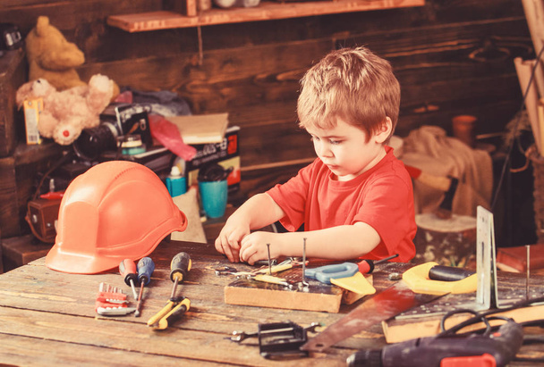 Toddler on busy face plays with tools at home in workshop. Kid boy play as handyman. Child cute and adorable playing with tools as builder or repairer, repairing or handcrafting. Childhood concept - Foto, afbeelding