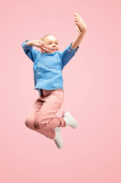 Young happy caucasian teen girl jumping with phone in the air, isolated on pink studio background. - Zdjęcie, obraz