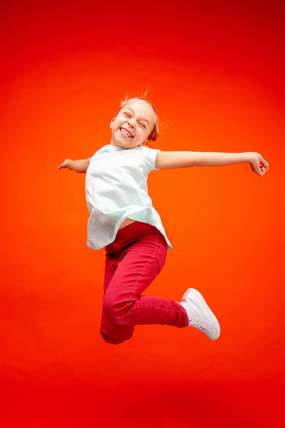 Young happy caucasian teen girl jumping in the air, isolated on red studio background. - Fotografie, Obrázek