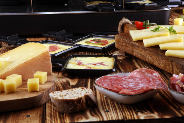 Delicious traditional Swiss melted raclette cheese served in individual skillets with salami - Photo, Image