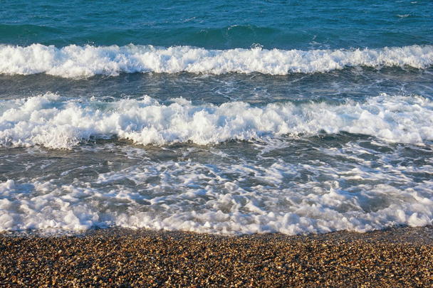 Líneas horizontales de olas blancas en una playa de guijarros en un día soleado y ventoso. Montenegro, Mar Adriático
 - Foto, Imagen