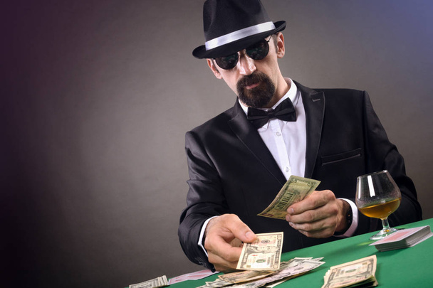 Elegant gentleman in tuxedo is gambling at the table on gray background. - Photo, Image