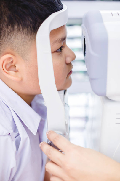 sprawdzenie wzroku. Chłopców azjatyckich sprawdzanie korekcji wzroku i widzenia. Leczenia i rehabilitacji. Pojęcie Klinika okulistyki - chłopiec robi sprawdzanie wzroku przez nowoczesne technologie elektroniczne - Zdjęcie, obraz