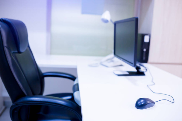el ordenador está sobre la mesa en un interior luminoso. escritorio gerente blanco y silla giratoria negro con ordenador PC y ratón en la oficina
. - Foto, Imagen