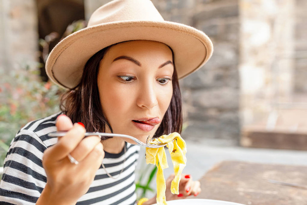 nuori aasialainen matkustava nainen syö italialaista pastaa vanhassa kaupungissa ulkona ravintolassa
 - Valokuva, kuva