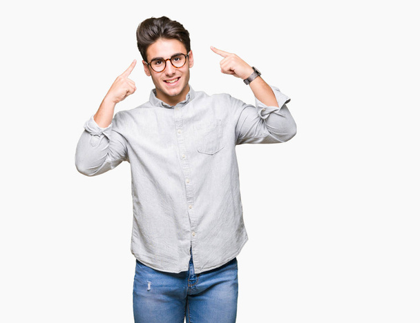 Όμορφος νεαρός φορώντας γυαλιά πάνω από απομονωμένες φόντο χαμογελώντας επισημαίνοντας κεφάλι με δύο χέρια δάχτυλο, μεγάλη ιδέα ή σκέψη, καλή μνήμη - Φωτογραφία, εικόνα