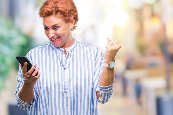 Atrractive senior caucasienne rousse femme textos à l'aide d'un smartphone sur fond isolé crier fier et célébrer la victoire et le succès très excité, acclamer l'émotion
 - Photo, image