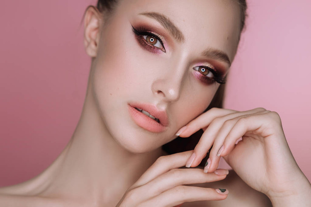 portrait of a beautiful elegant brunette girl with makeup and haircut in the studio on a pink background - Photo, Image