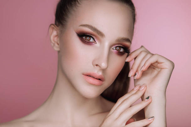 portrait of a beautiful elegant brunette girl with makeup and haircut in the studio on a pink background - Foto, Imagen