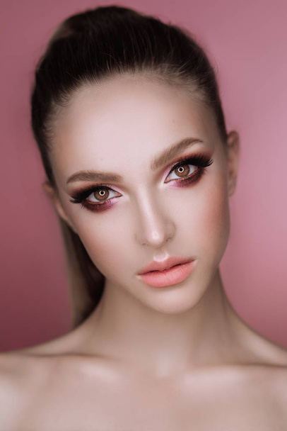 portrait of a beautiful elegant brunette girl with makeup and haircut in the studio on a pink background - Φωτογραφία, εικόνα