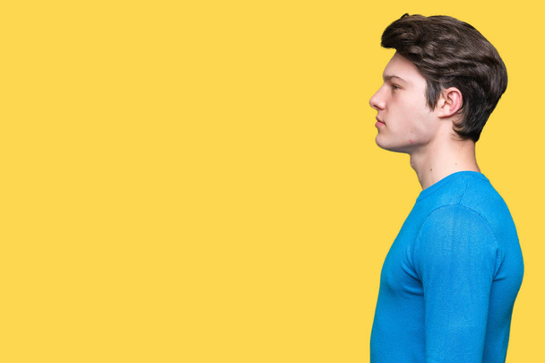Mladý pohledný muž na sobě modrý svetr izolované pozadí pohledu na stranu, uvolnit profilu pozice s přirozenou tvář s sebejistý úsměv. - Fotografie, Obrázek