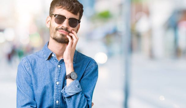 Young handsome man wearing sunglasses over isolated background thinking looking tired and bored with depression problems with crossed arms. - Foto, afbeelding