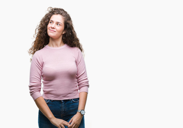 Beautiful brunette curly hair young girl wearing pink sweater over isolated background smiling looking side and staring away thinking. - Fotó, kép