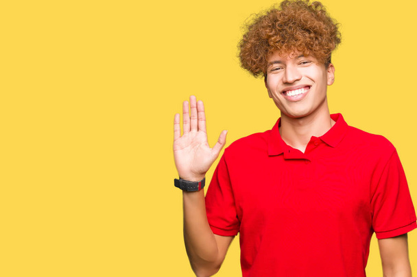 junger gutaussehender Mann mit Afro-Haaren in rotem T-Shirt, der darauf verzichtet, fröhlich und lächelnd Hallo zu sagen, freundliche Begrüßungsgeste - Foto, Bild