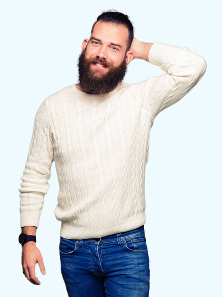 Молодой хипстер в зимнем свитере, уверенно улыбающийся, прикасающийся к волосам жестом руки вверх, позируя привлекательным
 - Фото, изображение
