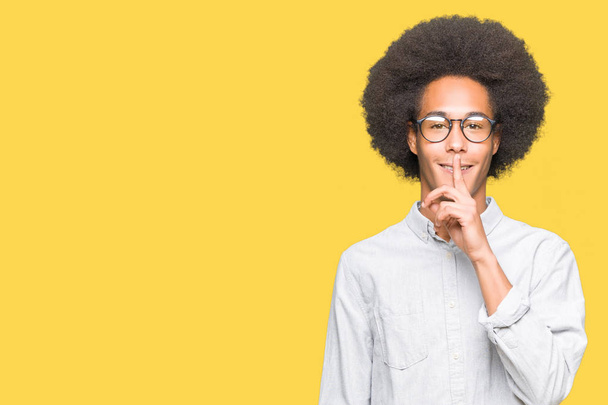 Молодий афроамериканець людиною з афро волосся в окулярах просять, щоб бути спокійним пальцем на губах. Мовчання і секретний концепції. - Фото, зображення