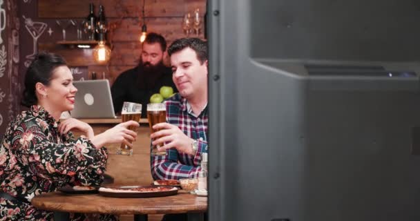 Kaukasisches Paar vor dem Fernseher in der Kneipe. Sie lachen und haben Spaß beim Bier trinken und Erdnüsse essen - Filmmaterial, Video