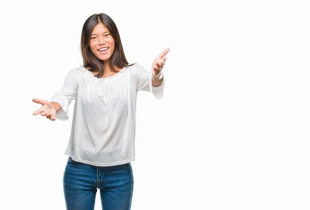 Młoda Azjatka kobieta na białym tle patrząc na kamery, uśmiechając się z otwartymi ramionami na uścisk. Ogarnięcie szczęście wesoły wyrażenie. - Zdjęcie, obraz