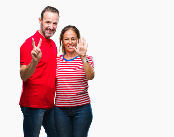 Μέση ηλικία Ισπανόφωνος ζευγάρι στην αγάπη πέρα από το απομονωμένο υπόβαθρο δείχνει και δείχνει προς τα επάνω με τα δάχτυλα αριθμός επτά ενώ χαμογελώντας αυτοπεποίθηση και χαρούμενοι. - Φωτογραφία, εικόνα